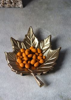 a leaf shaped brooch with nuts in it on a gray tableclothed surface