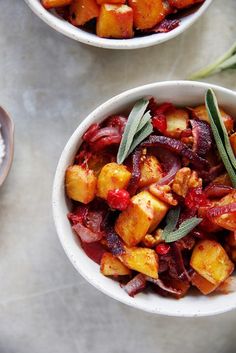 two white bowls filled with food on top of a marble counter topped with green leaves