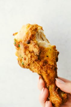 a person holding up a piece of fried chicken with cheese and chives on it