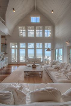 a living room filled with lots of white furniture and large windows overlooking the water in front of it