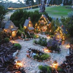 a miniature garden with lights in the shape of houses on rocks and gravel, surrounded by trees