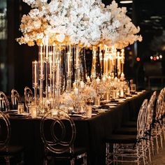 a long table is set with clear chairs and tall centerpieces filled with white flowers