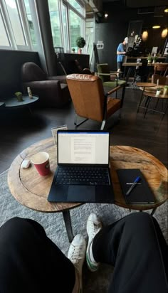 a laptop computer sitting on top of a wooden table next to a person's legs