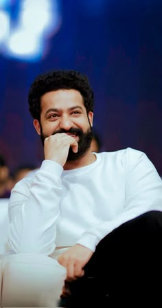 a man sitting down with his hand on his chin and looking at the camera while smiling