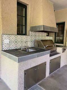 an outdoor kitchen with stainless steel appliances and tile backsplash, windows, and doors