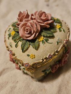 a heart shaped box with pink roses on it sitting on a cloth covered tablecloth