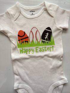 a white baby bodysuit with an image of baseballs and eggs on it that says happy easter