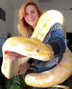 a woman holding a large yellow snake in her arms