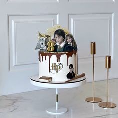 a harry potter themed birthday cake on a white pedestal with gold candles and decorations around it