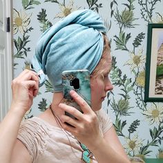 a woman with a towel on her head is looking at her cell phone in the mirror