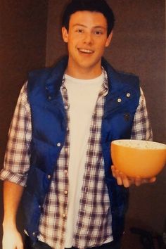 a man is holding a bowl and smiling at the camera while wearing a blue vest