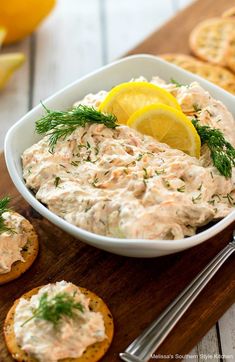 a white bowl filled with dip next to crackers and lemon wedges