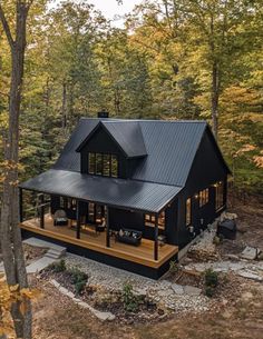 a black cabin in the woods with lots of trees and rocks on the ground around it