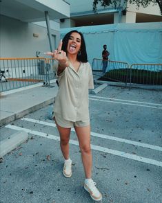 a woman standing in the middle of a parking lot with her hand up and smiling