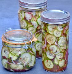 three jars filled with pickled cucumbers on a blue tableclothed surface