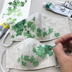 a person is painting leaves on a cloth face mask with markers and glue, along with other crafting supplies