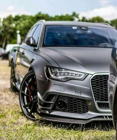 the front end of a grey car parked on top of a grass covered field next to other cars