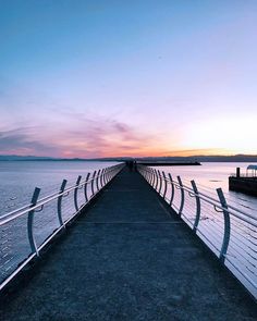 a long pier stretching out into the water at sunset or dawn with people walking on it