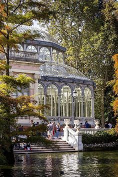 people are sitting on the steps in front of a building with a glass roof that is surrounded by trees and water