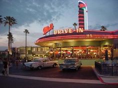 the drive - in movie theater is lit up at night with palm trees and parked cars