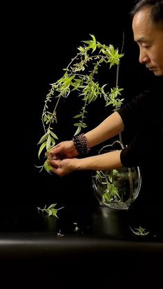 a man is holding plants in a glass vase on a black table with dark background