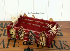 a red wooden box filled with small houses and birds on top of a wood floor