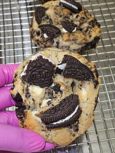 two cookies with oreos and cream fillings are on a cooling rack, one is being held by a gloved hand