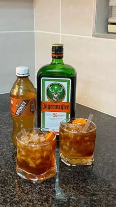 two glasses filled with liquid next to an empty bottle and another glass on the counter