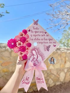 a person holding up a pink and white graduation cap with flowers in front of a stone wall