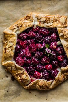 a pie topped with berries and almonds on top of parchment paper