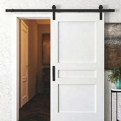 an open white door with a black handle on the wall next to a potted plant