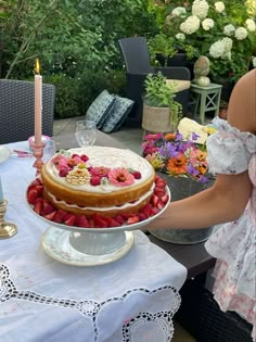 a woman is holding a cake with strawberries on it and candles in the background