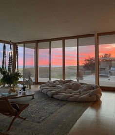 a living room filled with furniture and large windows overlooking the ocean at sunset or dawn