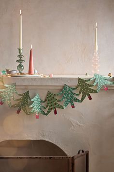 a mantle with candles and paper trees on it in front of a fireplace mantel