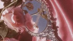 a mirror sitting on top of a table next to flowers and a red cloth covered wall