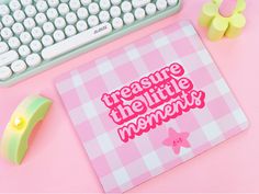 a pink mouse pad sitting next to a keyboard on top of a desk with the words,'treasure the little moments'printed on it