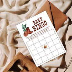 a baby shower game sitting on top of a bed next to an envelope and pen