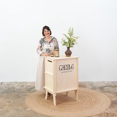 a woman standing next to a wooden cabinet with a potted plant on top of it