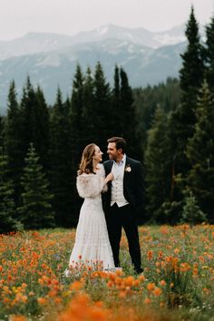 a bride and groom standing in a field full of wildflowers with mountains in the background