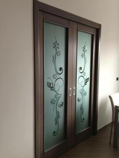 two glass doors with designs on them in a room next to a table and chair