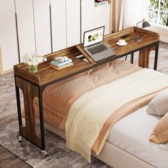 a laptop computer sitting on top of a wooden desk next to a bed with pillows