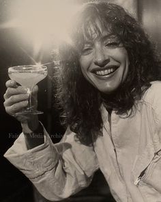 black and white photograph of a woman holding a drink in her right hand while smiling at the camera