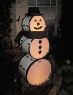 a snowman made out of drums in front of a house with the lights on