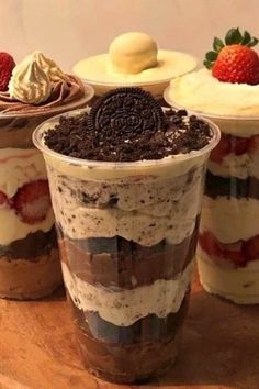 three desserts in plastic cups on a wooden table with strawberries and oreo cookies