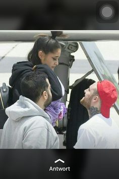 a man with a red hat is talking to two other people in front of an airplane