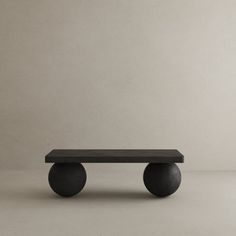 a black bench sitting on top of a cement floor next to a white wall with two round legs