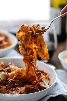 a person holding a fork full of pasta with meat and cheese on it in a white bowl