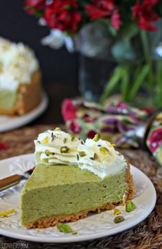 there is a slice of green cake on the plate and flowers in the vase behind it