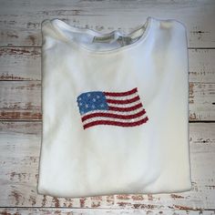 a white shirt with an american flag embroidered on the front and back, sitting on a wooden surface