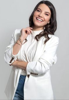 a smiling woman in a white jacket and jeans posing for the camera with her arms crossed